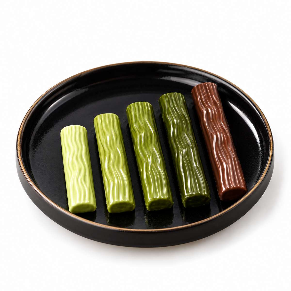 Vier matcha chocolade sticks in verschillende tinten en een hojicha stick op een zwart bord