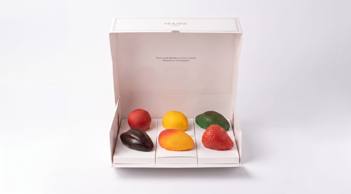 Open doos met zes mousse cakes in fruitvorm: framboos, mango, pistache, chocolade, passievrucht en aardbei